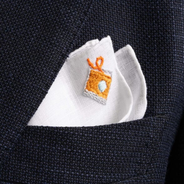 A white linen pocket square with hand-embroidered old-fashioned cocktail detailing
