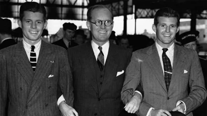 JFK with father and brother wearing adark on light chalk stripe with striped knit tie and collar pin