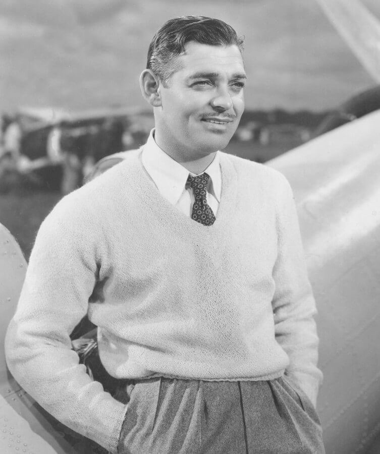 Clark Gable wearing a v-neck sweater and a printed tie micropattern tie with grey pleated high rise pants