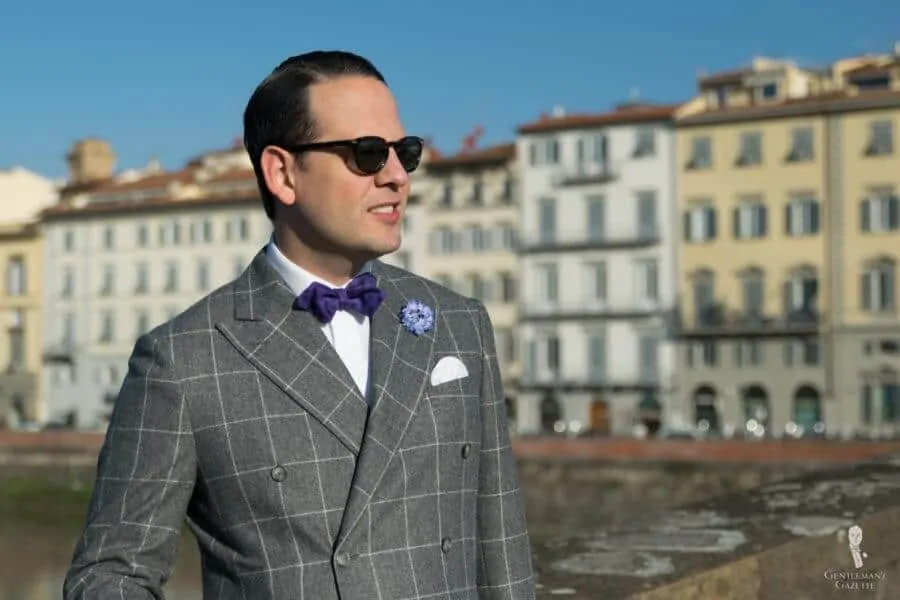 Sven Raphael Schneider wearing a DB suit with an Ancient Madder Silk Bow Tie in Purple Paisley, Blue Cornflower Boutonniere, and Pocket Square in White Irish Linen 