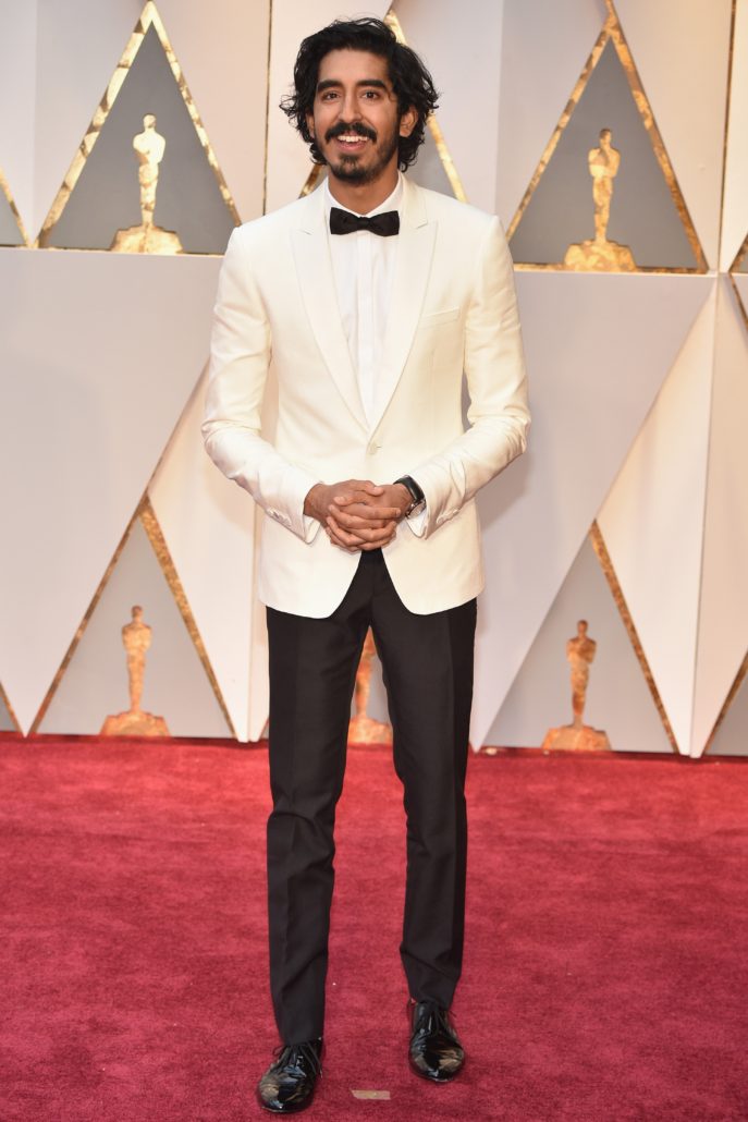 Dev Patel with off white Dinner Jacket, hidden fly shirt and slim bow tie with patent leather shoes