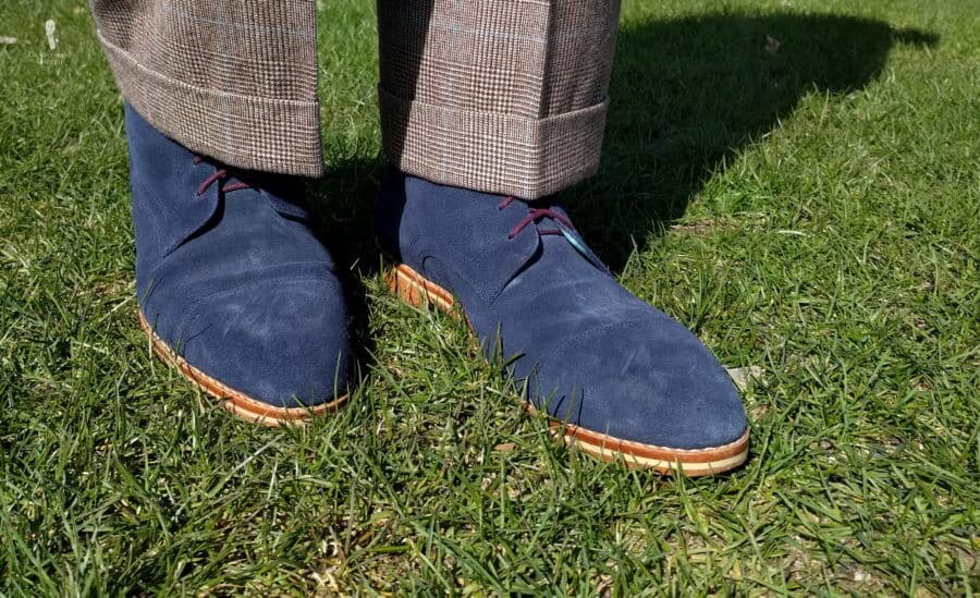 Brown windowpane cuffed pants paired with blue suede boots on green lawn