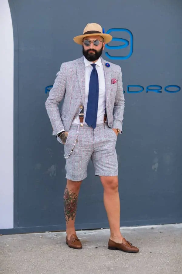 The shorts suit with blue tie, suspenders, buttoniere, pocket square, hat, sunglasses and tassel loafers