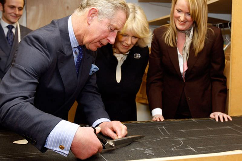 The Prince of Wales tries his hand at cutting a wool fabric for a suit