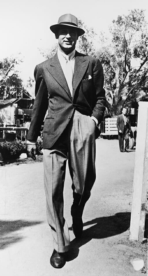 British born actor Cary Grant (1904 - 1986) walking outdoors wearing a pinstripe jacket and a hat, 1940s