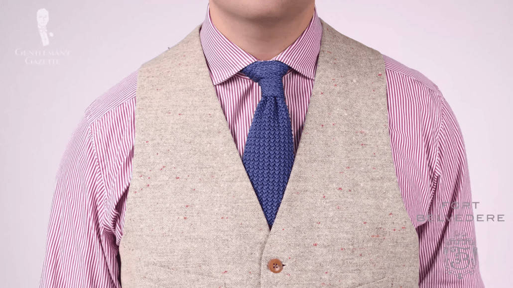 Red and white dress shirt paired with a vest and blue knit tie.