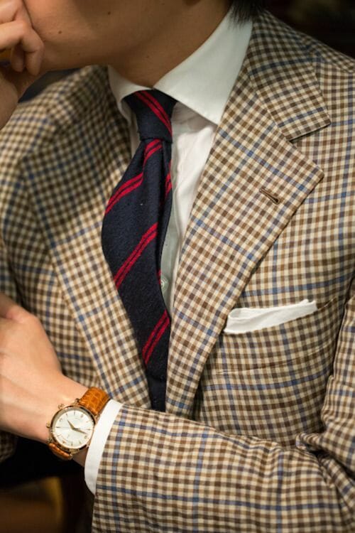 A gun club check jacket, a plain white shirt and pocket square and a blue and red stripe tie.