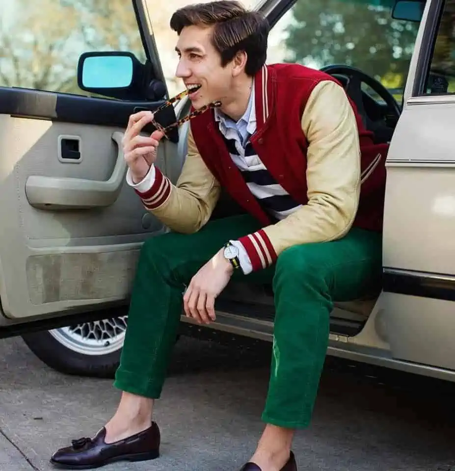 F.E. Castleberry of Unabashedly Prep wearing a varsity jacket, ocbd, rugby shirt, green chinos, and tassel loafers without socks