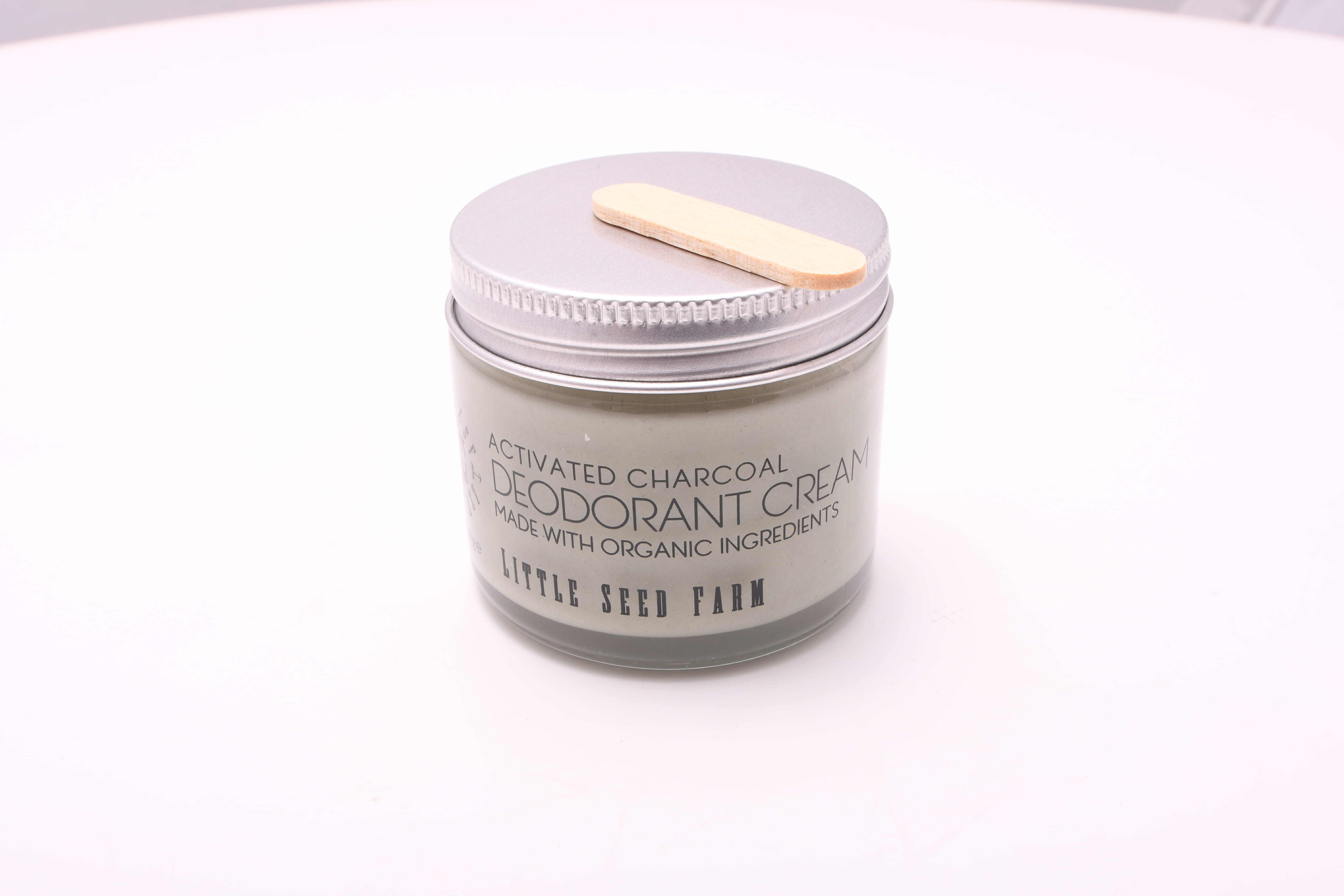 A jar of cream deodorant, made with activated charcoal and applied with the small wooden applicator.