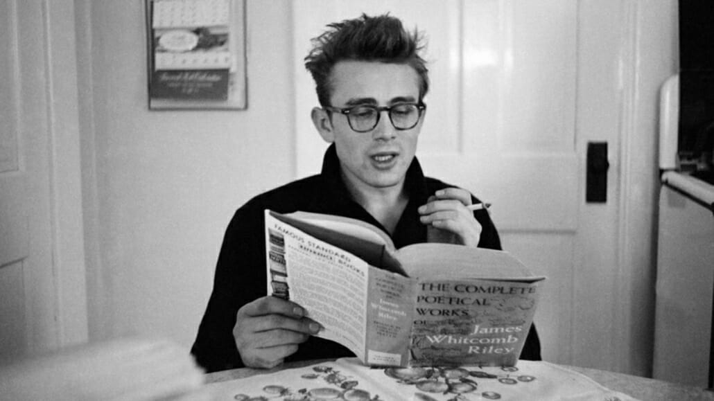 Dean wears a pair of tortoise-shell eyeglasses to read a book of poetry.