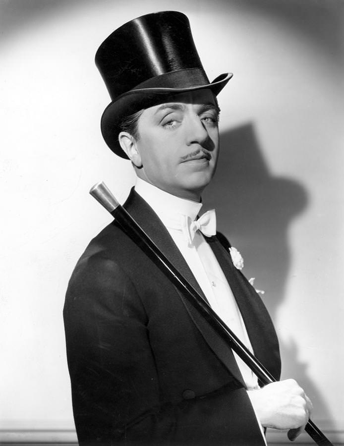 William Powell in shawl collar tailcoat, boutonniere, wing collar, with cane and silk top hat