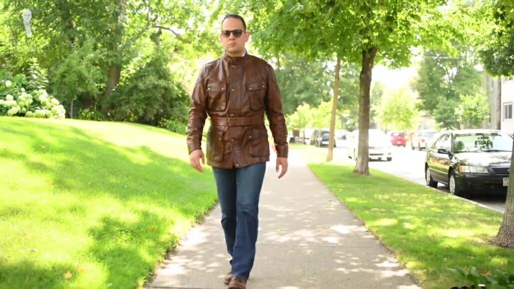 Raphael walking outdoors while wearing a brown Trialmaster Panther, denim jeans, brown boots, and sunglasses