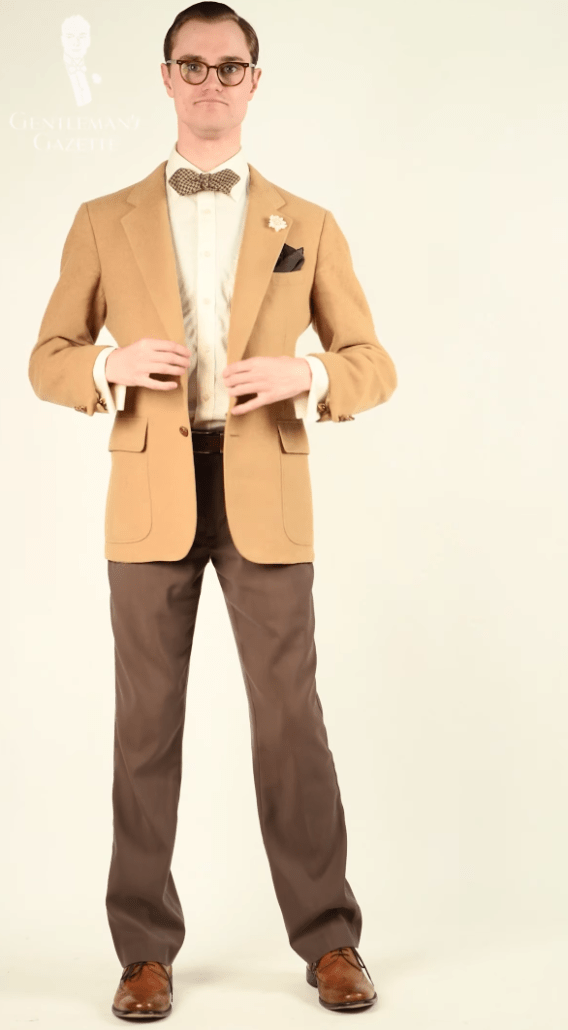 Preston wearing an off-white shirt, camel sport coat, and brown pants.