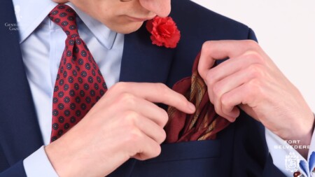 A blue suit worn with various red accessories like a boutonniere, tie, and pocket square