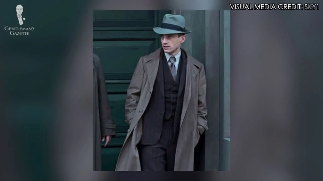Gereon Rath wearing a three-piece suit, overcoat, and a Fedora hat