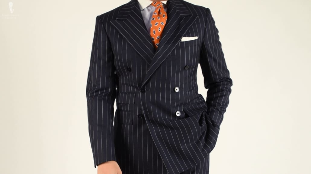 A double breasted navy pinstripe suit paired with a white pocket square and orange patterned tie. 