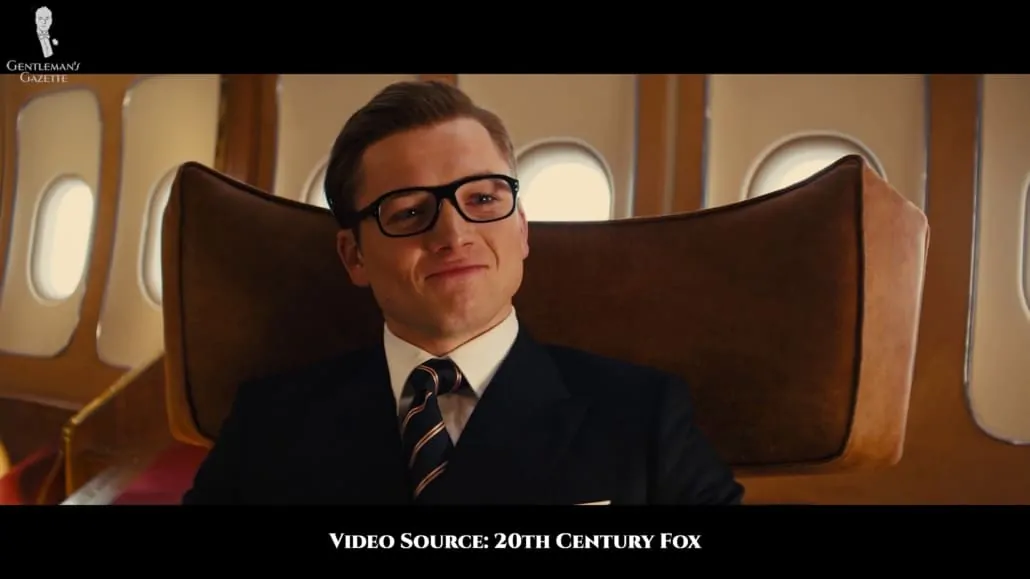 Eggsy wearing a plain navy suit, white shirt and his blue, pink, and brown rep tie.