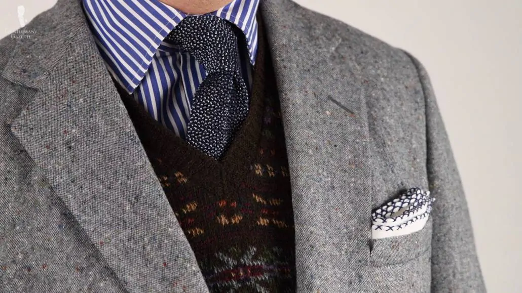 Gray Donegal jacket with a Fair Isle sweater, a blue shirt with white stripes, and a white linen pocket square with blue cross stitches along the edges and a dark blue and light blue two tone silk knit tie.