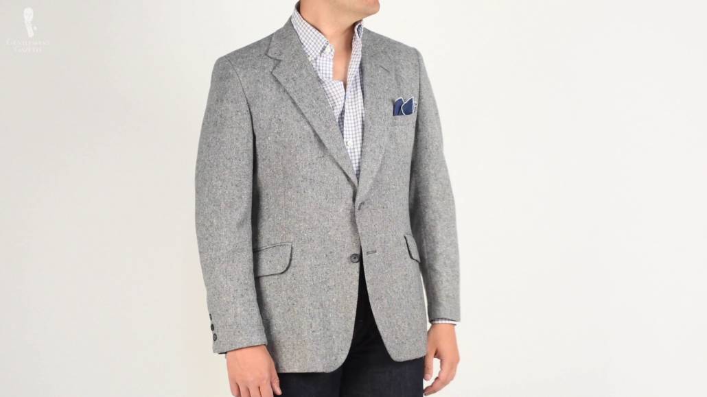 Gray Donegal tweed jacket with a white shirt with blue checks and a solid blue pocket square with a whitish string edge.