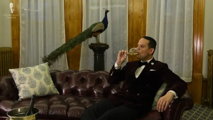 Raphael enjoying a glass of champagne in a black tie outfit while sitting comfortably on a Chesterfield sofa
