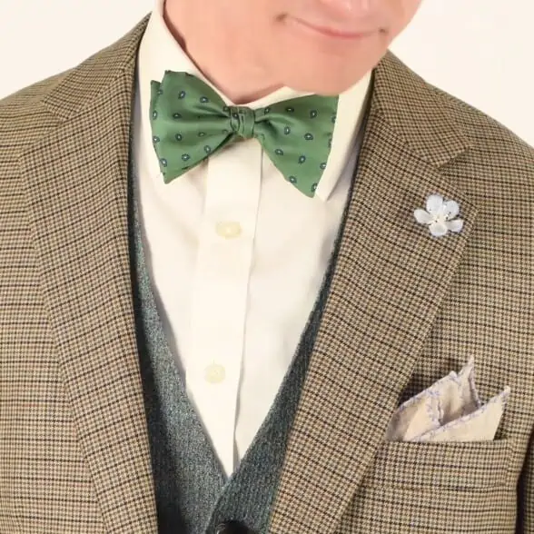 Houndstooth jacket paired with gray vest, white shirt, a light brown linen pocket square, light blue boutonniere and a green bow tie.