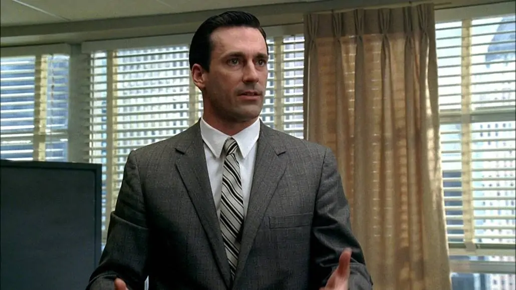 Don Draper in a light gray suit, striped tie, and white dress shirt