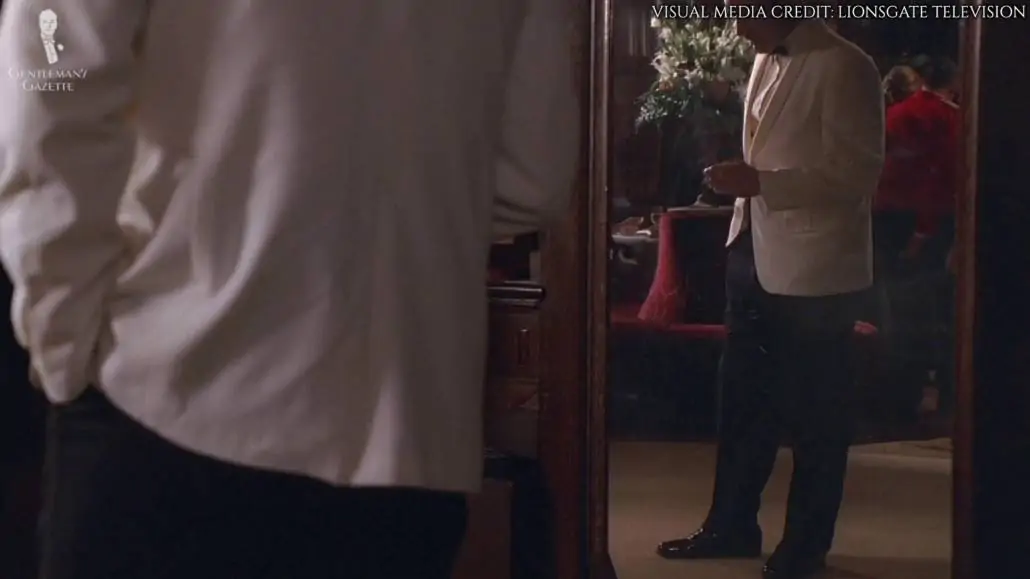A reflection in the mirror showing Don Draper wearing a black trouser and a black shoes with his dinner jacket.