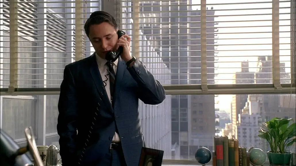 Pete Pete Campbell in a lighter-than-navy blue suit with two buttons and skinny lapel with a somewhat elevated gorge. He is currently standing up and talking on the telephone.