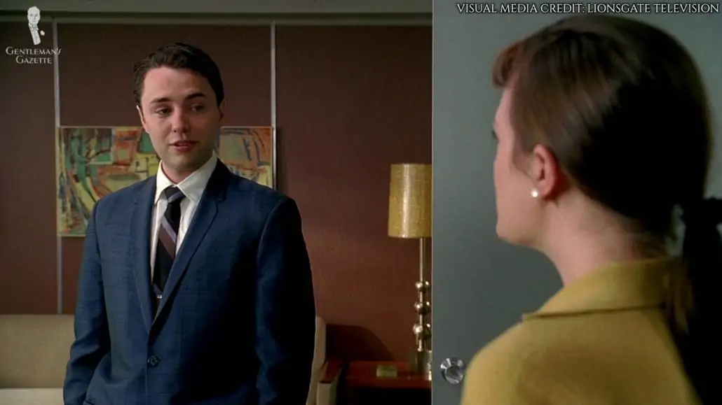 Pete Campbell wearing a mid-blue suit, white dress shirt with spread collars, and a striped tie. 