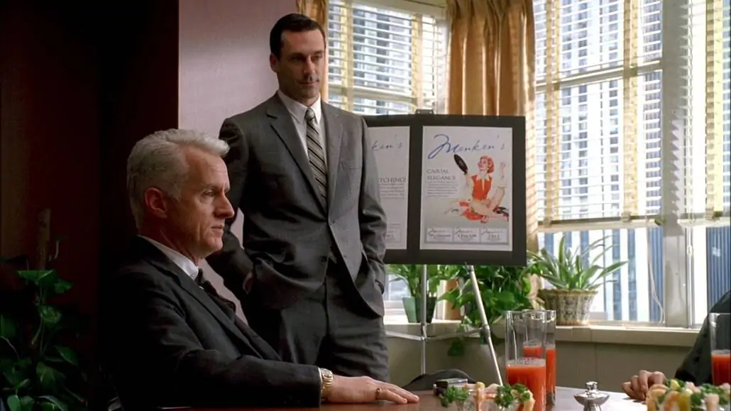 Don Draper standing beside a sitting Roger Sterling. Both are wearing business suits
