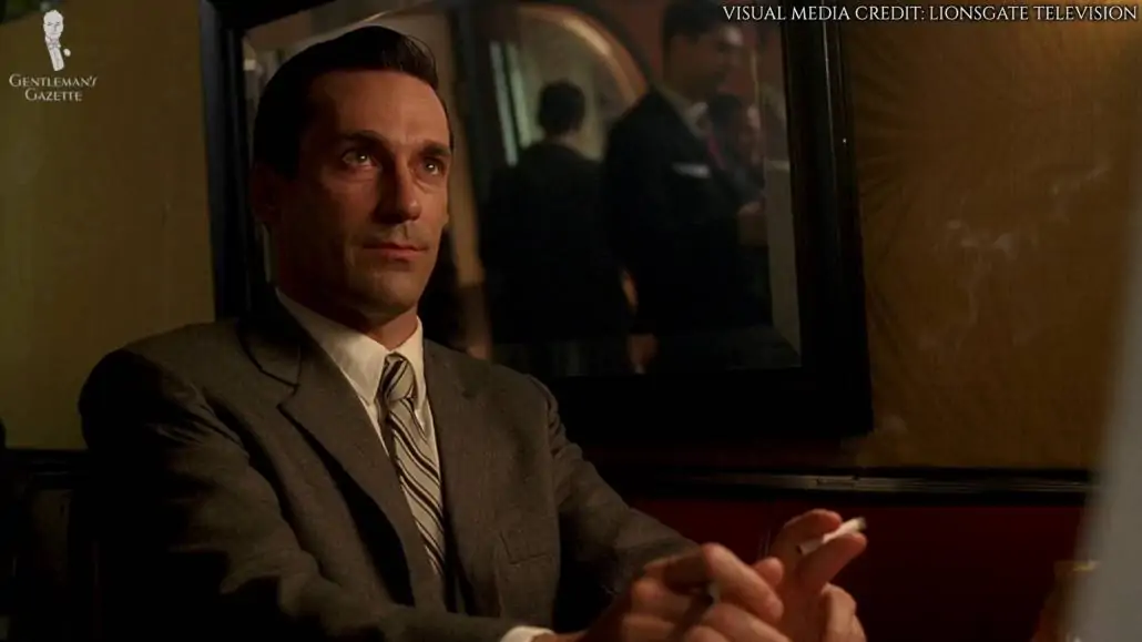Don Draper in a classic business suit with notched lapel. He's currently sitting and staring at the person he was talking to who was not included in this frame.