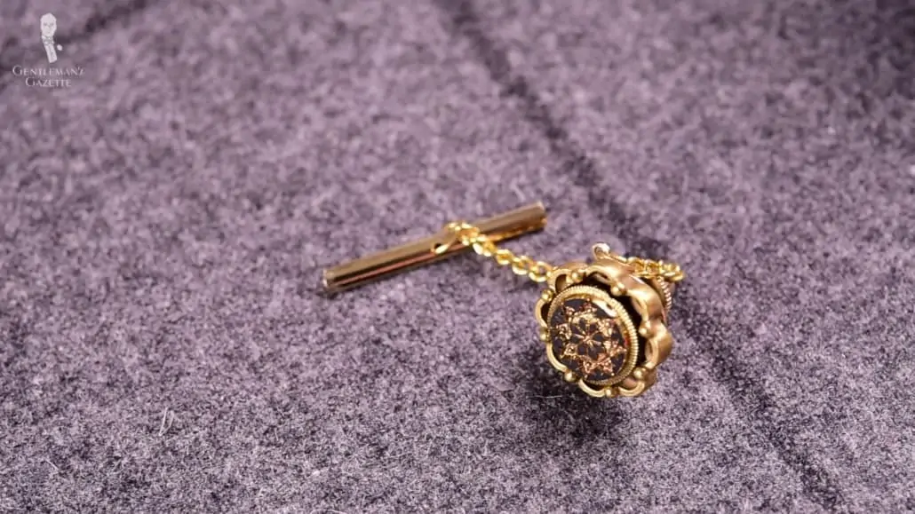 A gold tie tack attached on a t-bar