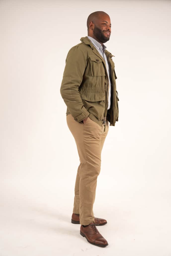 Kyle wearing a green field jacket with an off-white button-down shirt, chino pants, and brown dress shoes.