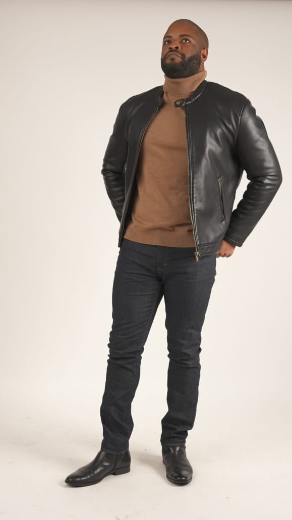 Kyle wearing a black waxed cotton leather jacket, tan turtleneck, denim, and boots.