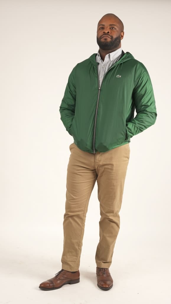Kyle sporting a green windbreaker jacket, dress shirt, khaki pants, and brown shoes. 