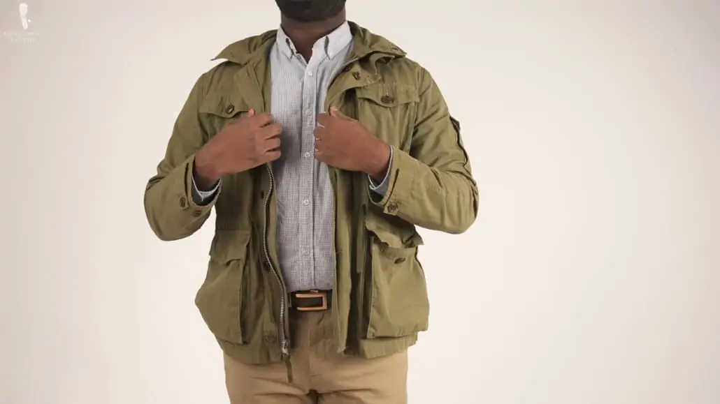 Kyle wearing een field jacket with an off-white button-down shirt, and chino pants.