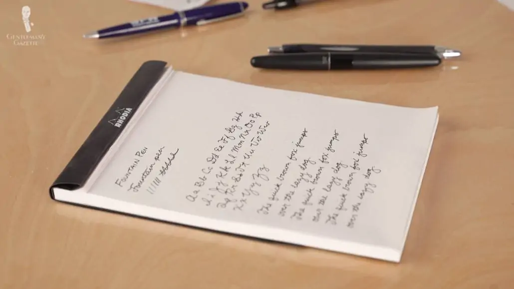 handwriting on a notepad with some fountain pens scattered on the side 