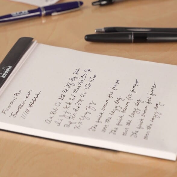 handwriting on a notepad with some fountain pens scattered on the side