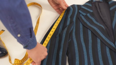 Raphael measuring a patterned suit jacket's sleeve length on the floor.