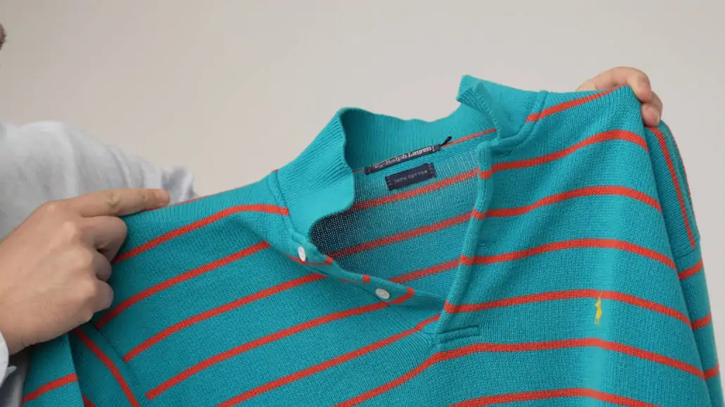 Raphael holding a turquoise knitted polo shirt with orange stripes