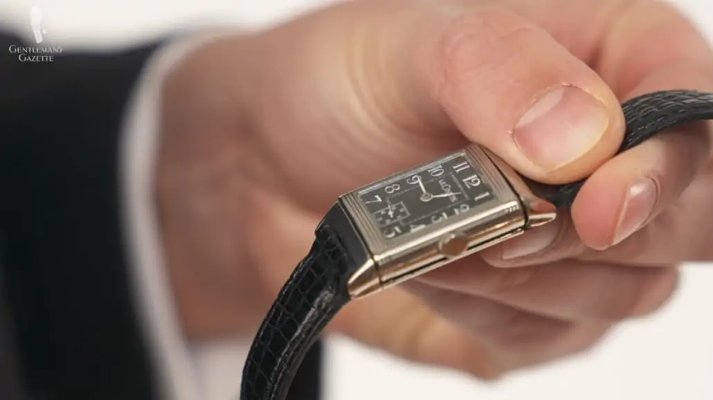 Raphael holding a Reverso watch with black leather straps, with a mechanical crown at the side 