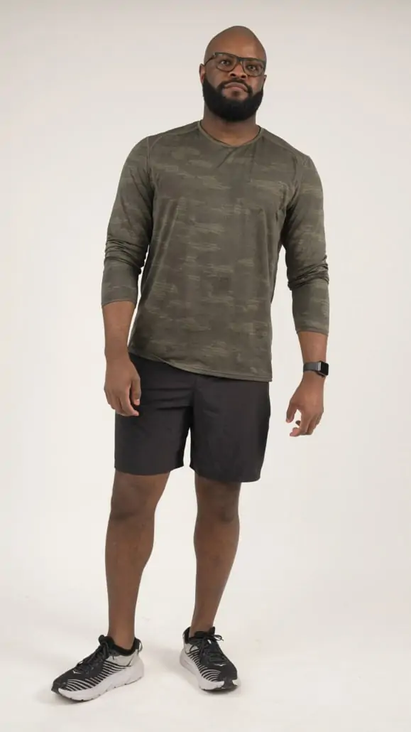 Kyle wearing a Black workout shorts and a long-sleeved camouflage workout shirt with black running shoes.
