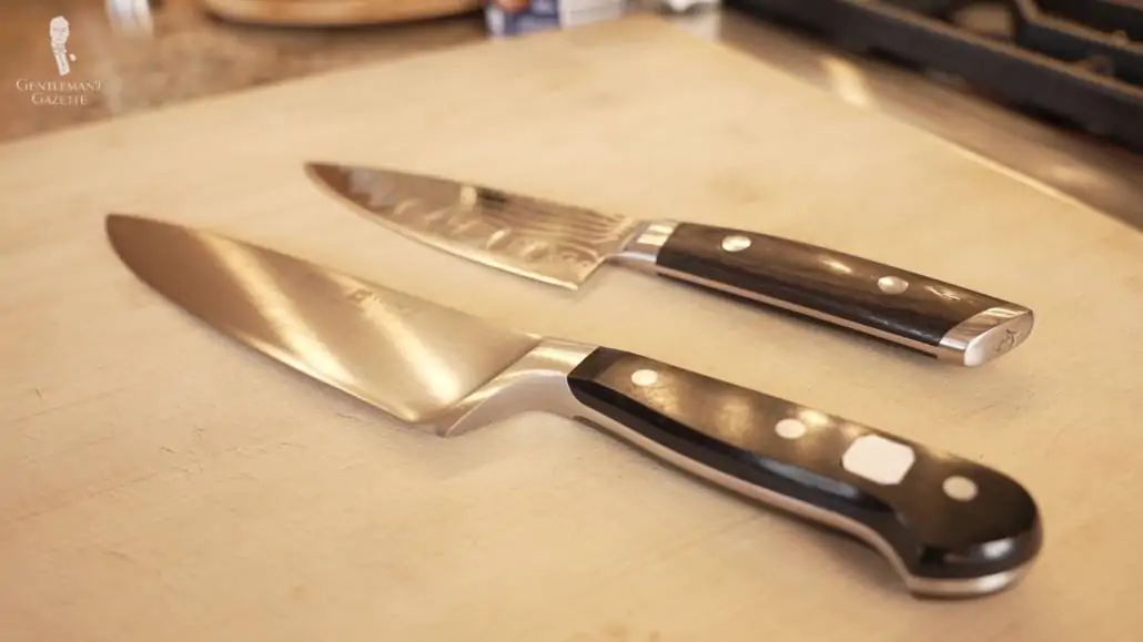 Two chef knives laid on top of a chopping board.