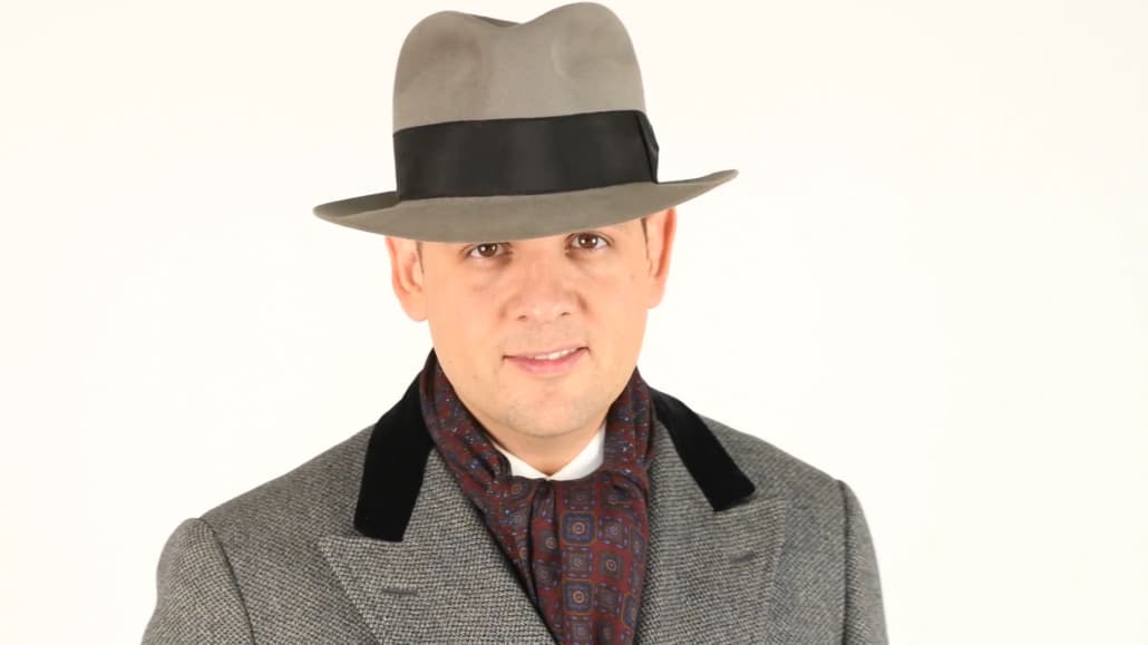 Raphael wearing a paletot overcoat with black velvet collar, light gray fedora with black band, and burgundy scarf