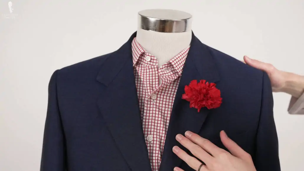 A natural carnation boutonniere on a navy suit jacket.