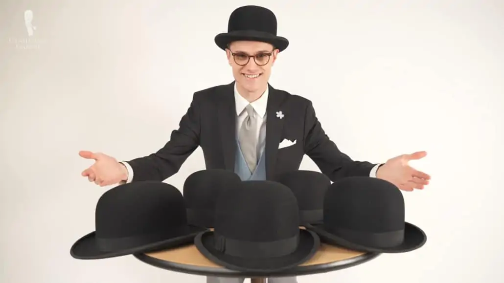 Preston wearing a stroller suit and a bowler hat. In front of him are bowler hats laid on top of a table.