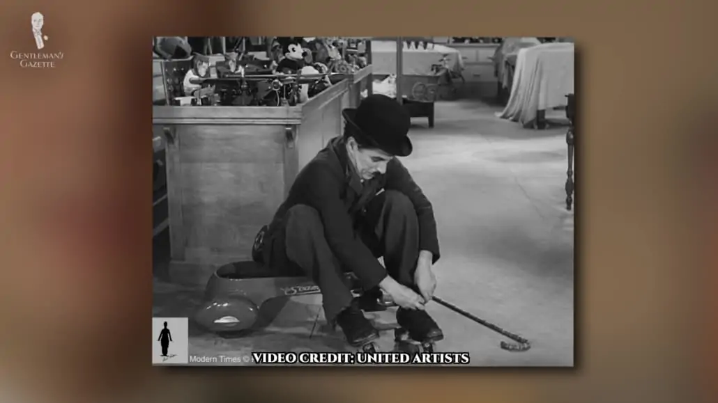 A scene from a film where Charlie Chaplin is fixing his roller blades. 
