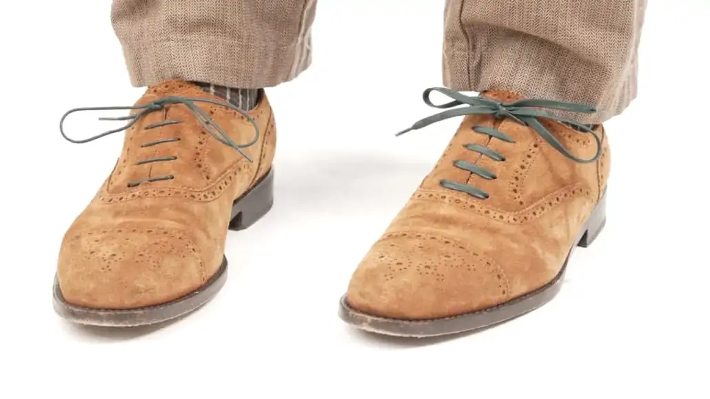 A tan oxford with dark green round shoelace on the right foot and dark green flat shoelace on the right.