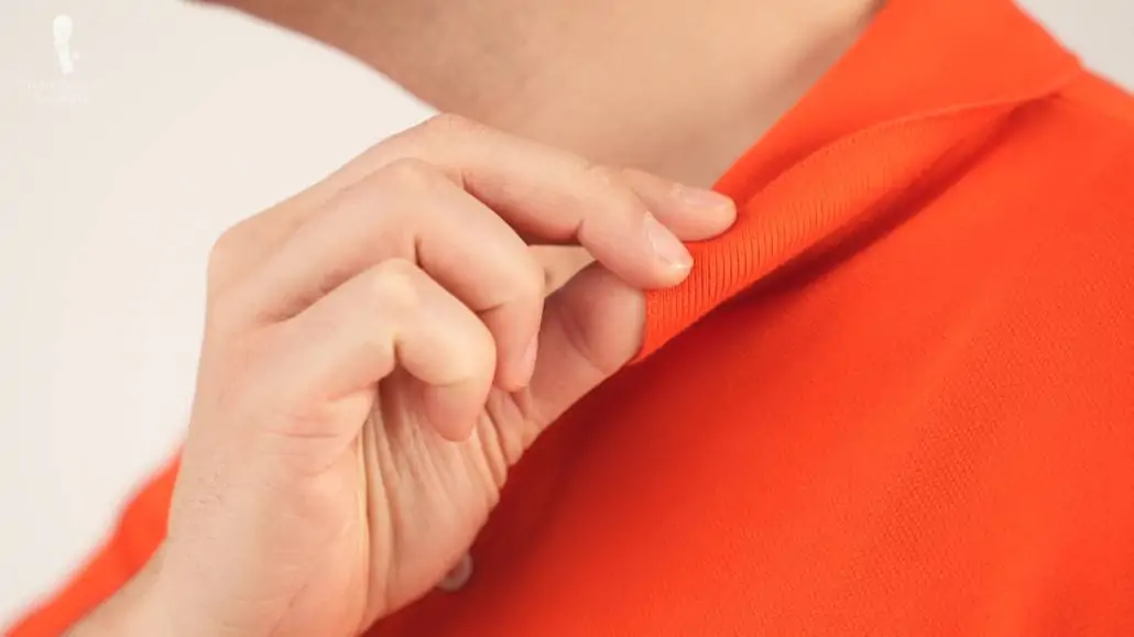 Raphael showing the ribbed collar of an orange Lacoste Polo Shirt. 
