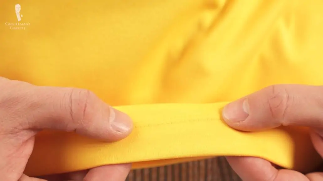 Raphael showing the stitch density of a yellow Lacoste polo shirt.